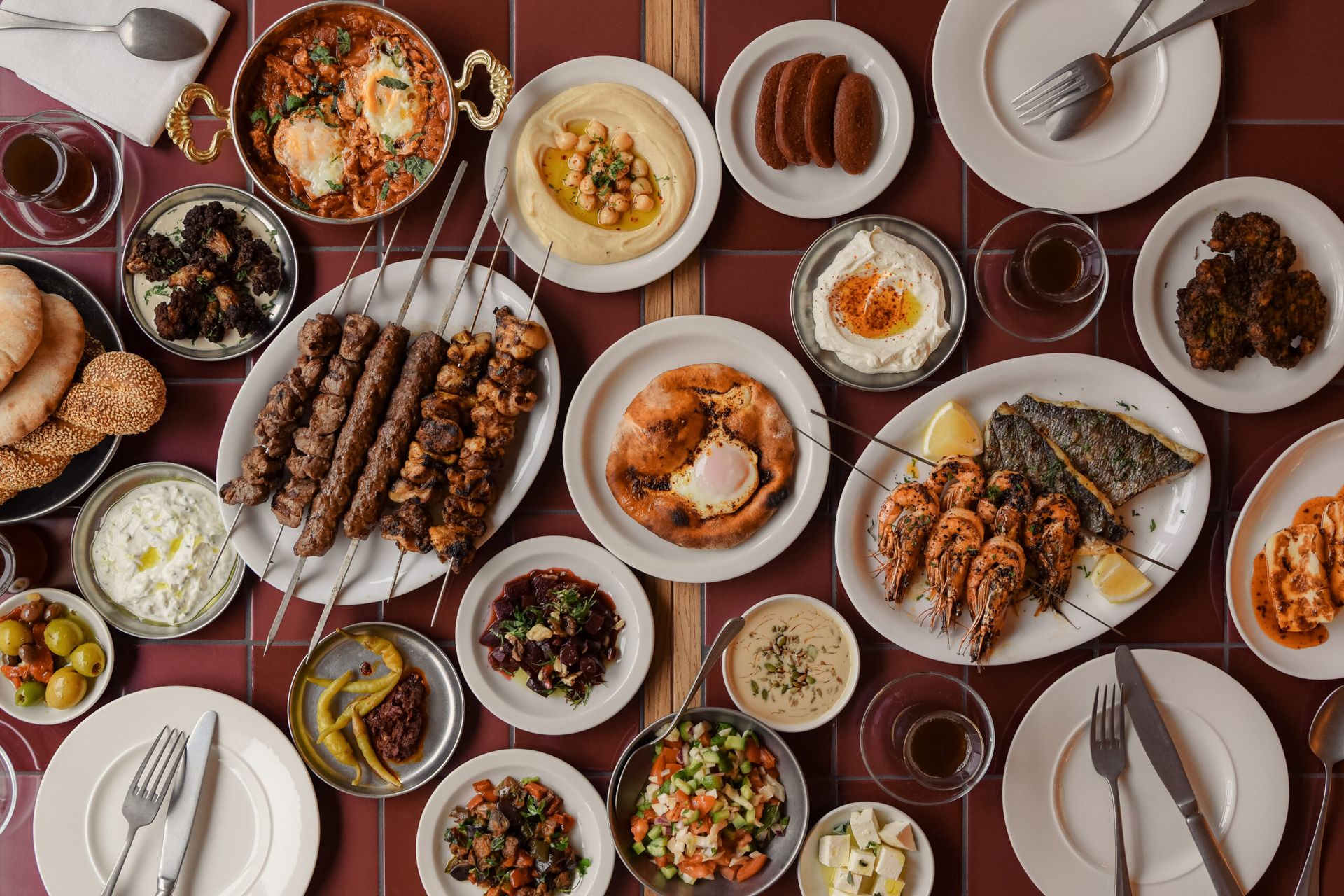 A table set for the weekend, featuring Middle Eastern dishes like grilled kebabs, houmous, salads, prawns, bread, dips, falafel, and drinks on white plates and bowls—perfect to fight the January blues.