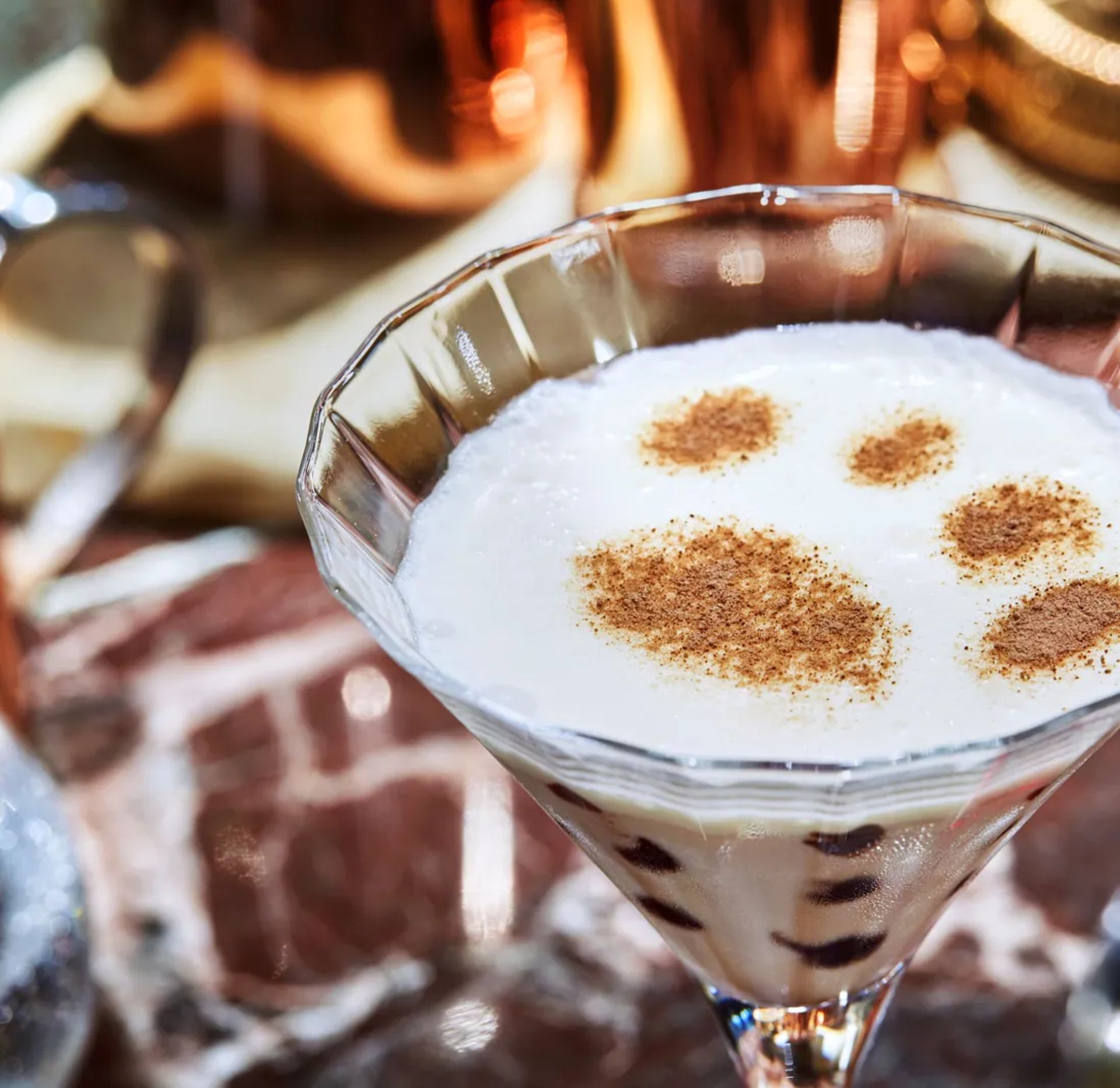 A martini glass filled with a creamy white cocktail, topped with cinnamon powder in the shape of a paw print, sits on marble—a playful nod to London winter drinks and cosy winter warmers.