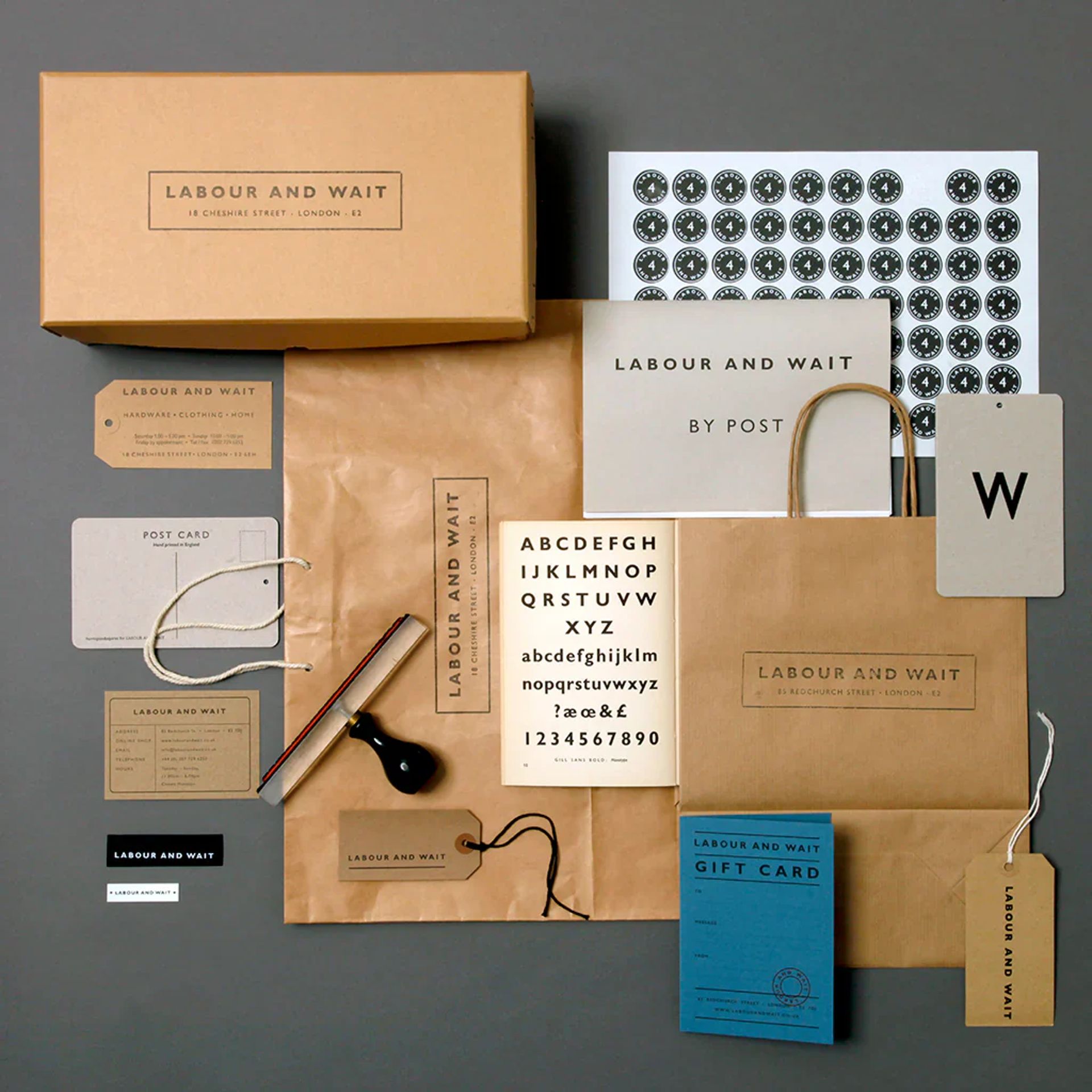 A flat lay of stationery and packaging items from Labour and Wait, evoking the charm of classic stationery shops, with boxes, bags, headed paper, envelopes, a rubber stamp, string, and alphabet sheets in neutral and kraft paper tones.