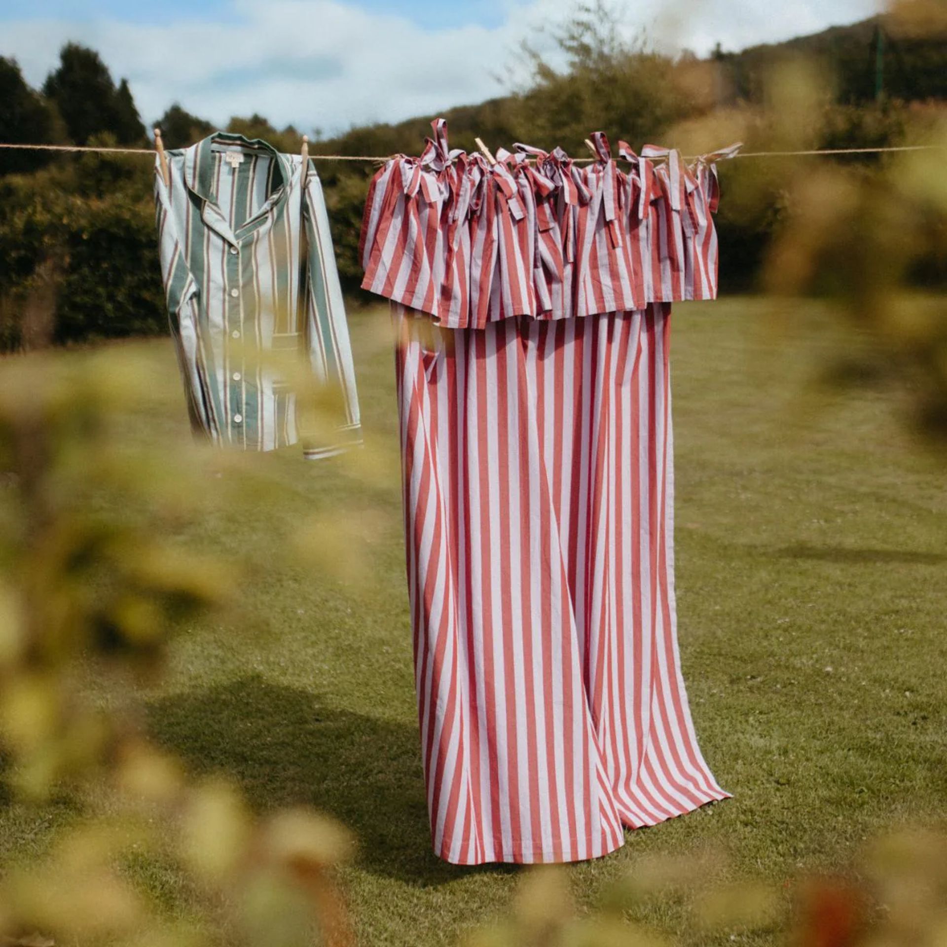Two sets of striped pyjamas hang on a washing line outdoors, with green grass and shrubs in the background under a partly cloudy sky—a scene reminiscent of tranquil mornings described in any good Insider’s Guide to Edinburgh.