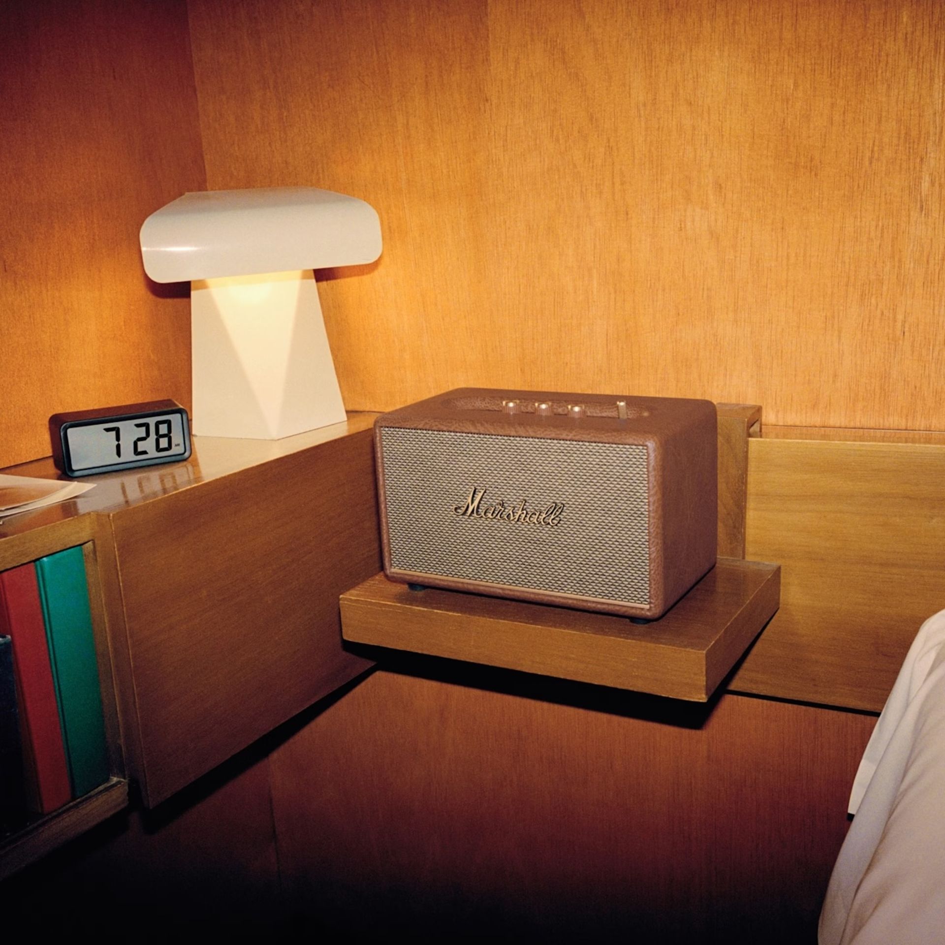 A Marshall speaker sits on a bedside shelf next to a digital alarm clock showing 7:28 and a modern desk lamp, perfect for listening room interior ideas.