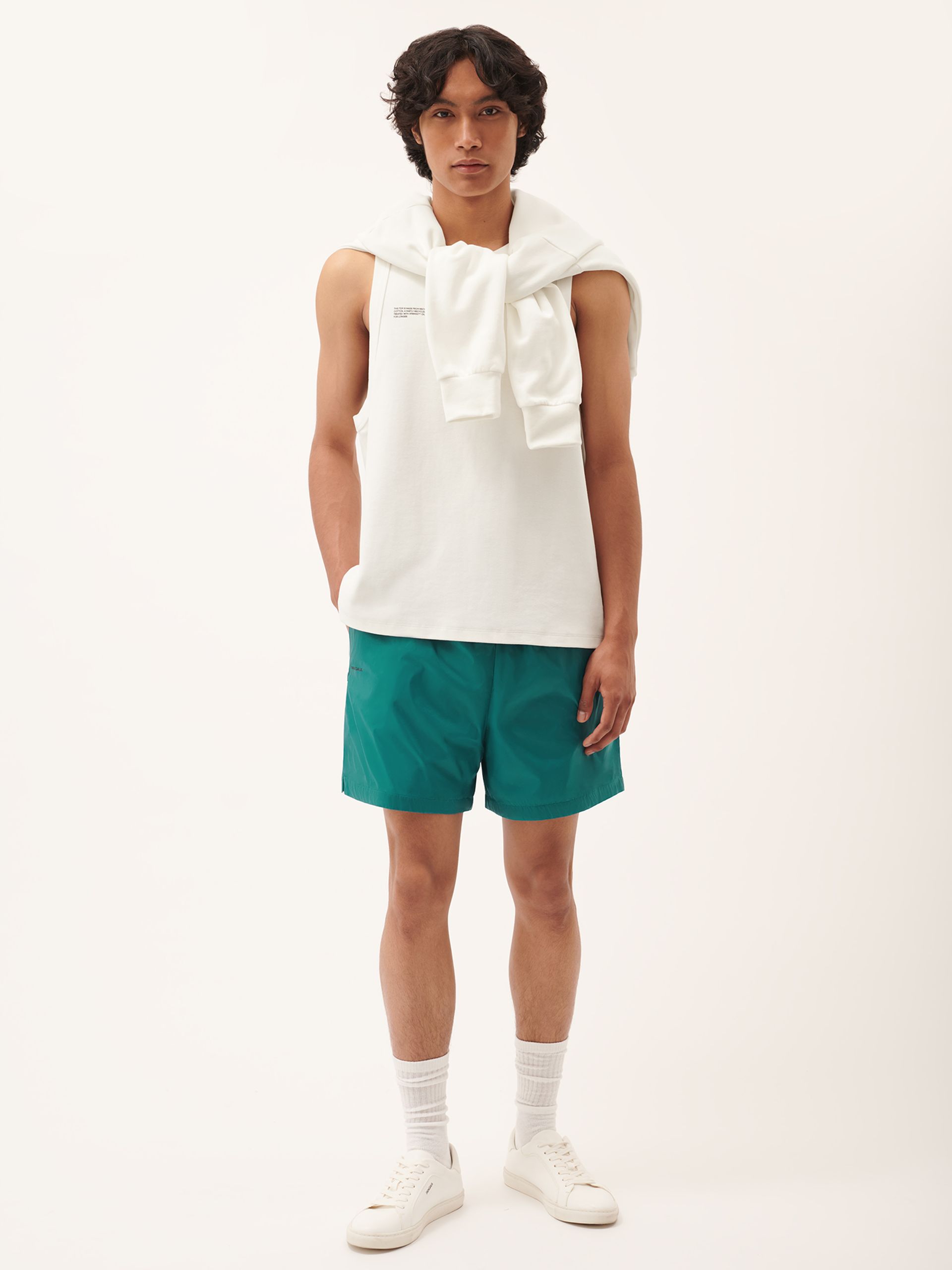 male model in white vest and teal nylon shorts by pangaia 