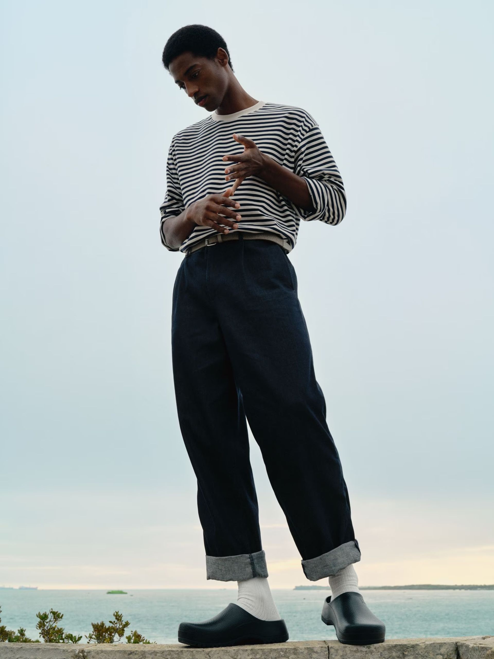 male model standing on sea wall wearing breton top and turned up jeans 