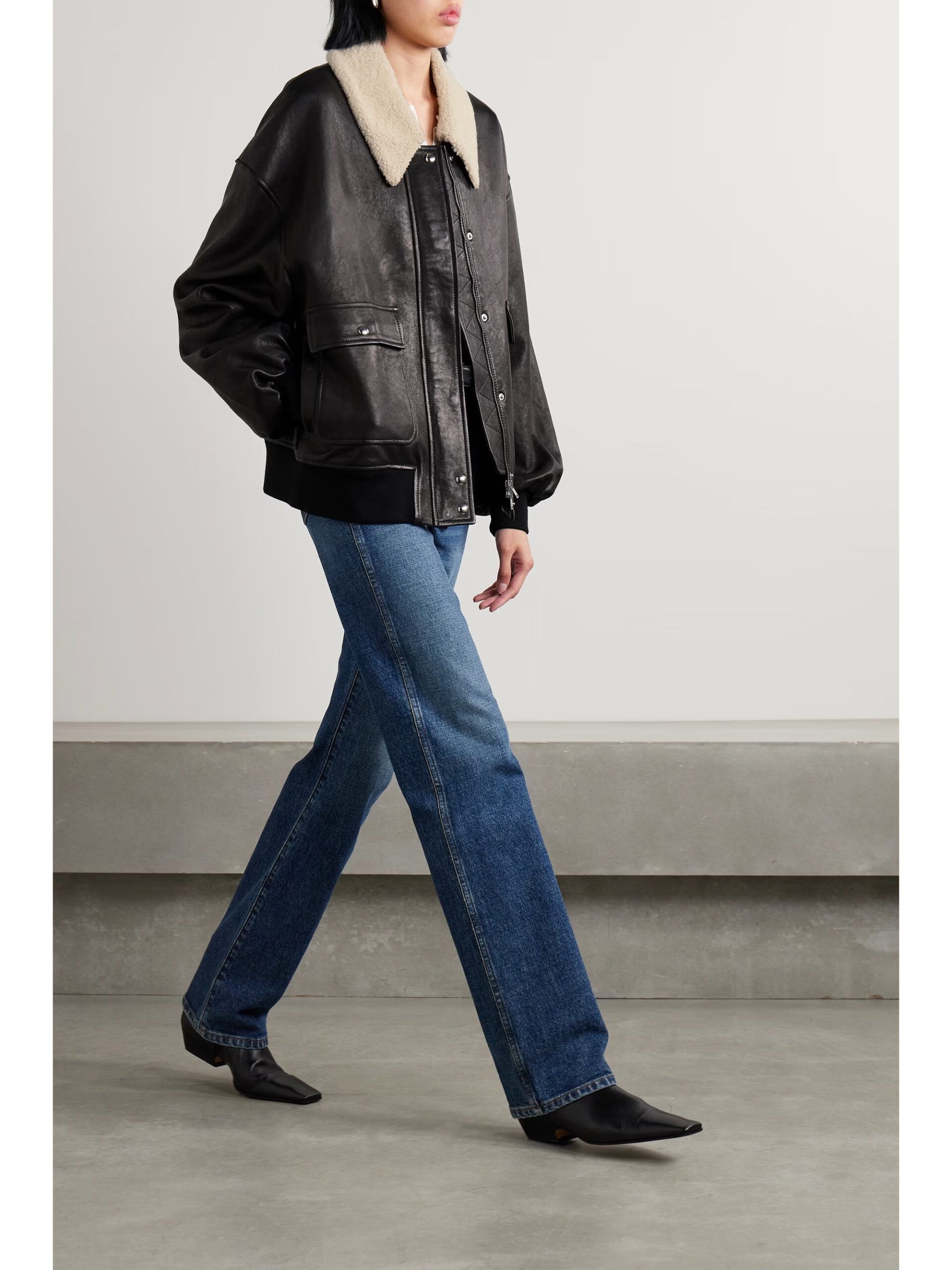 A person wearing one of the best women’s leather jackets with a faux-shearling collar, blue straight-leg jeans, and black pointed-toe boots.