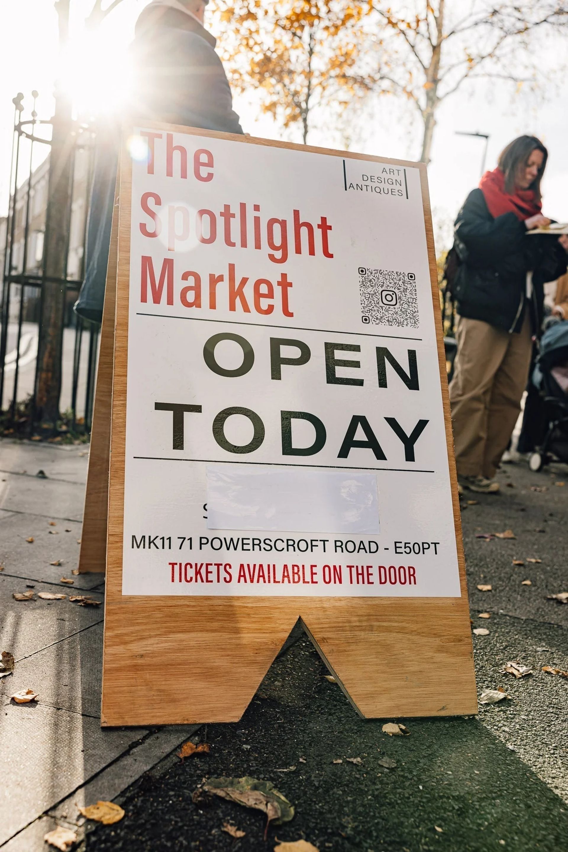 A sandwich board sign on a pavement reads “The Spotlight Market OPEN TODAY” with address details and “Tickets available on the door.” People and autumn trees are visible in the background, making it a standout stop in any London flea markets guide.