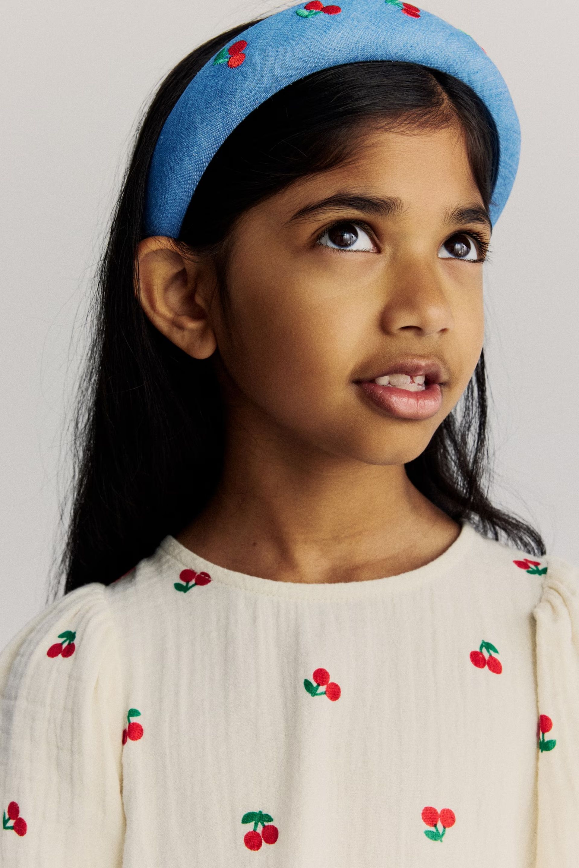 little girl headshot wearing cherry dress and blue headband 