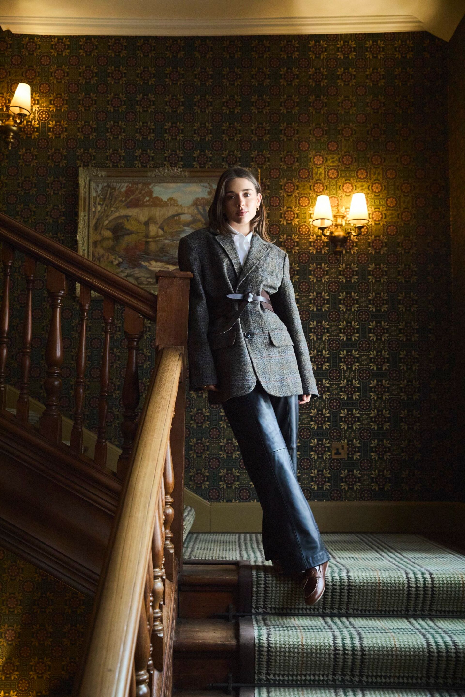 female model standing on stairs wearing harris tweed blazer and jeans