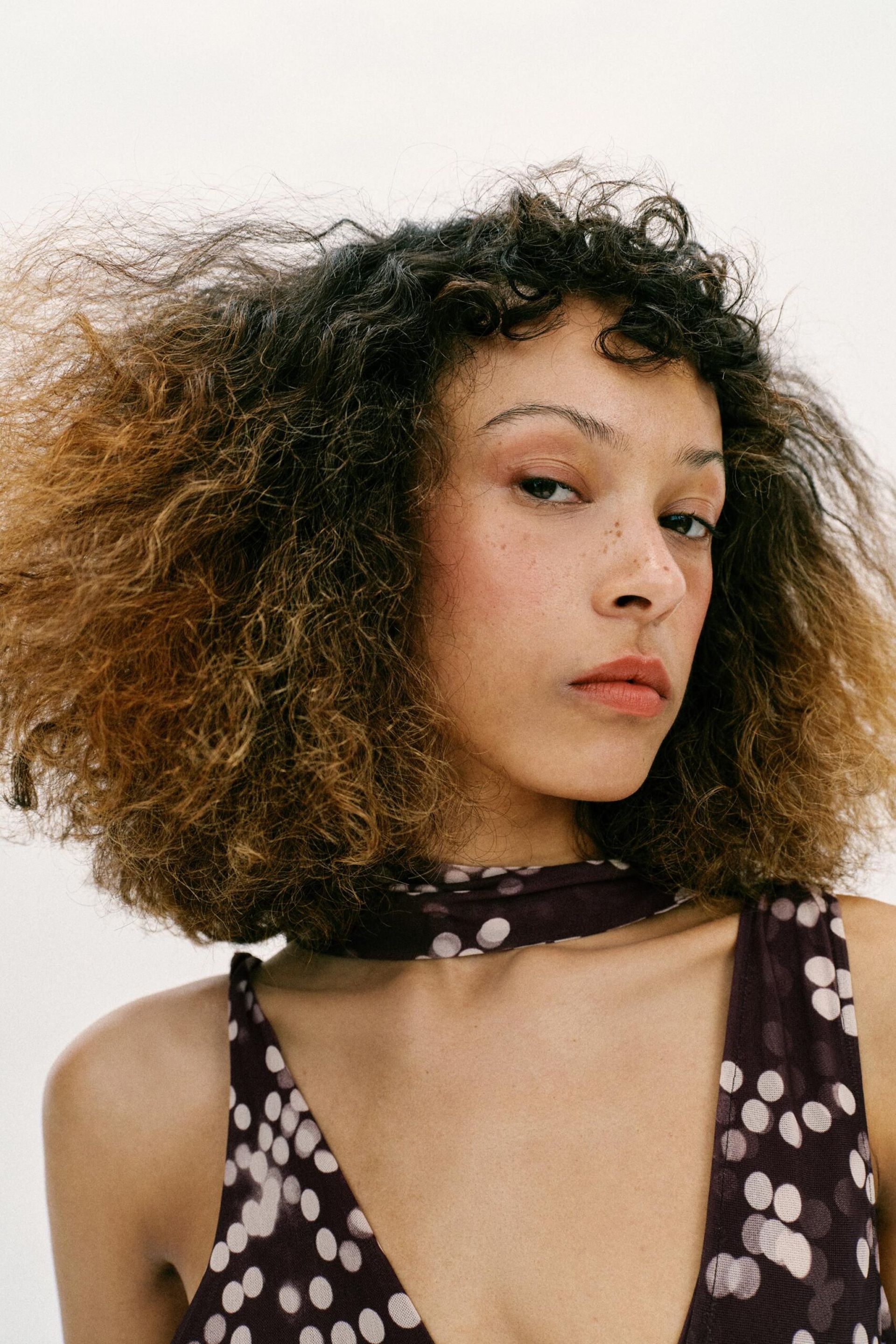 model close up with curly hair wearing spotty strappy dress with neck tie detail 
