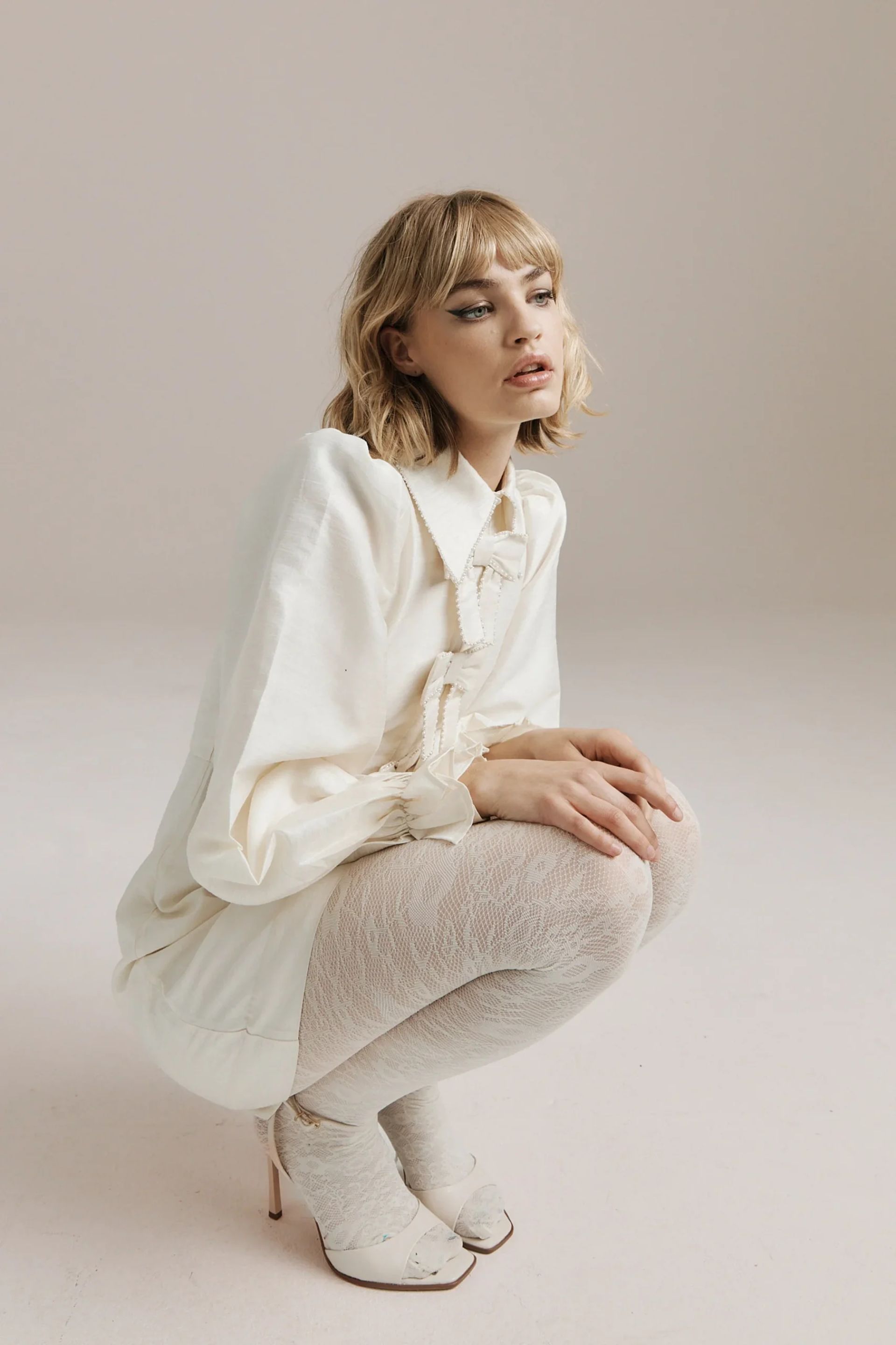 model wearing ivory dress with bows down the front, white tights and white shoes