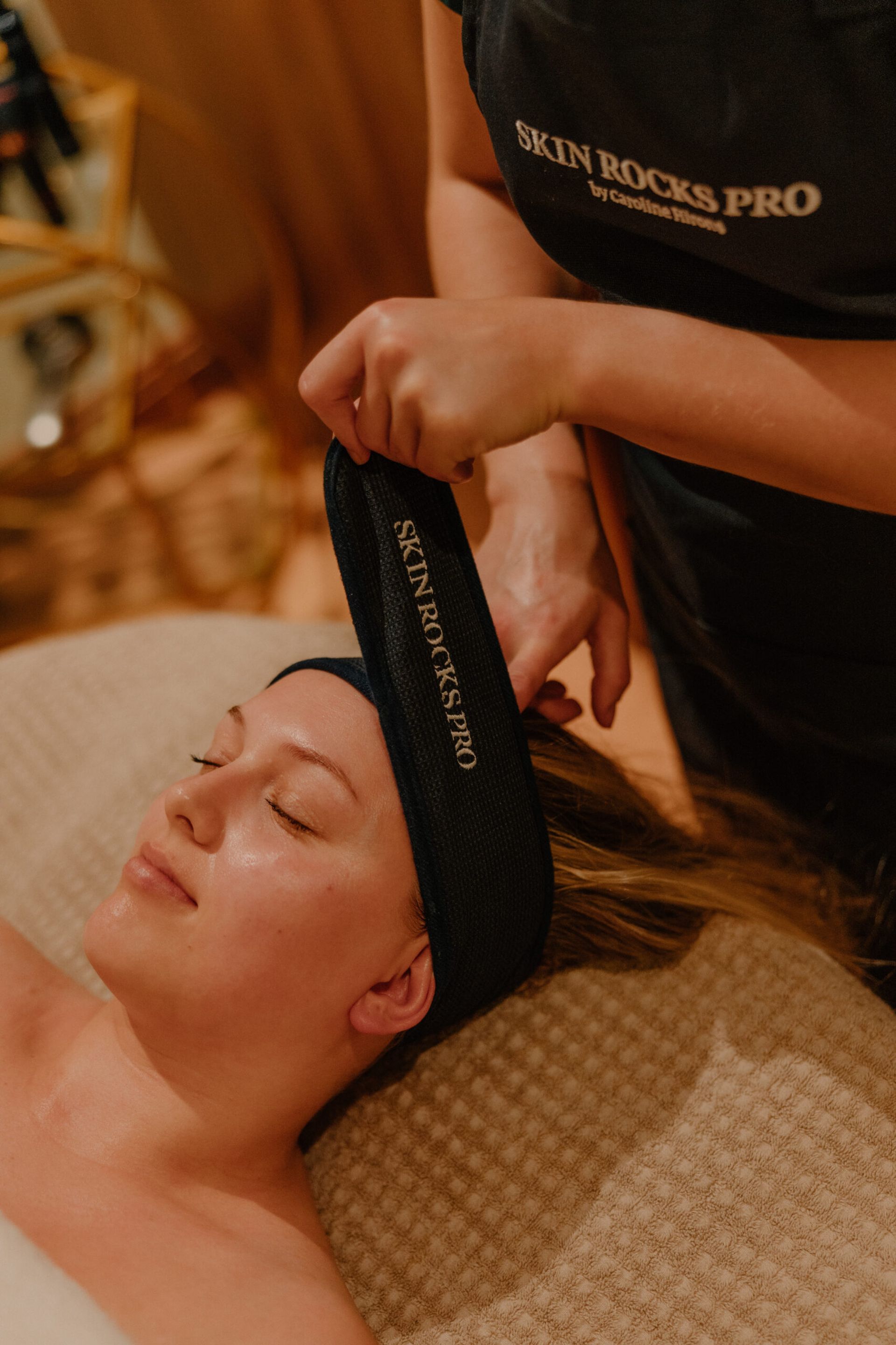 A person lies on a spa bed with eyes closed, while a professional in a Skin Rocks Pro apron secures a black headband labelled SKIN ROCKS.PRO around their head, evoking the pampering found at luxury hotels in Scotland.