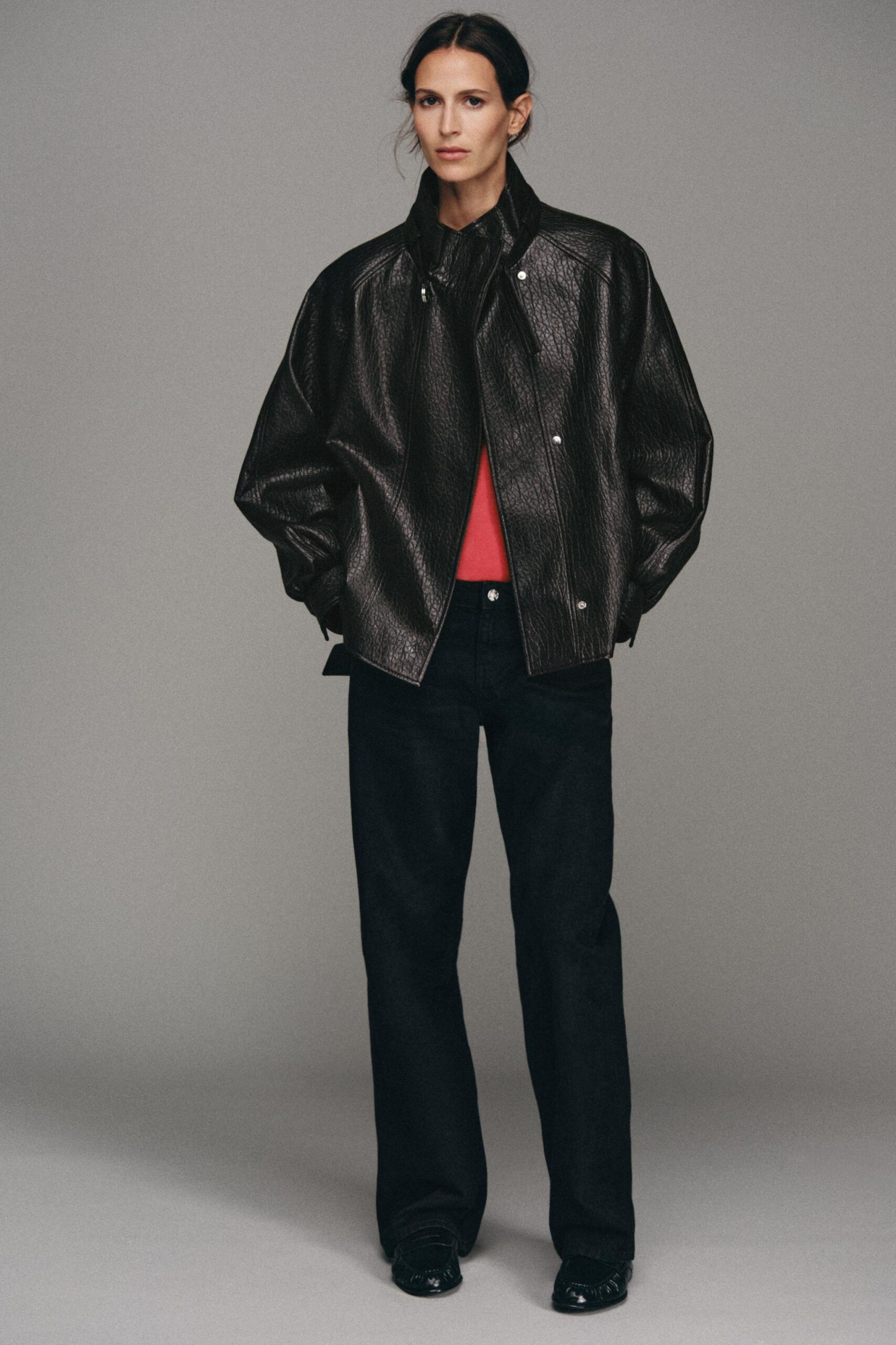 A woman wears one of the best women's leather jackets over a red top and black trousers, with her hands in her pockets.