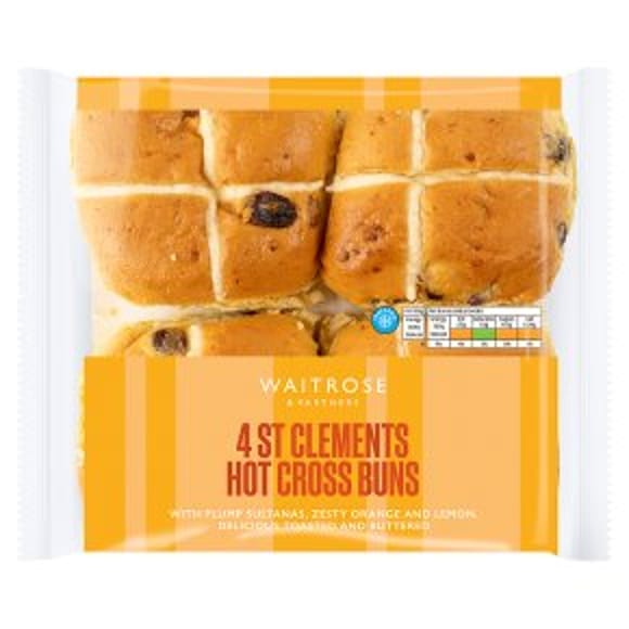A pack of four Waitrose St Clements hot cross buns in clear packaging, perfect for Easter entertaining. The golden buns feature visible currants and crosses, with a label highlighting their orange, lemon, and sultana ingredients.