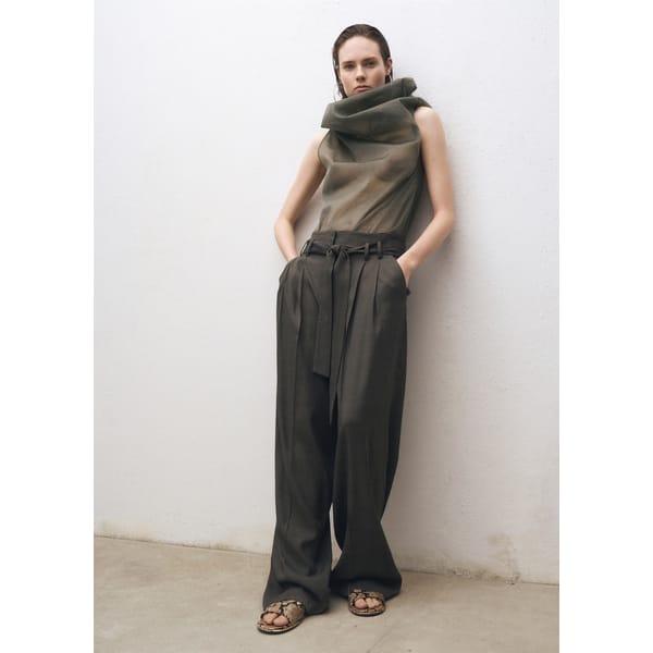 model leaning against wall wearing MANGO Silk blouse with asymmetrical neckline