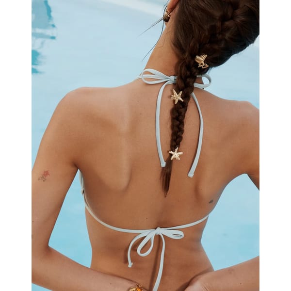 model in bikini from back wearing ASOS DESIGN pack of 4 mixed seashell starfish design hair claws in gold tone