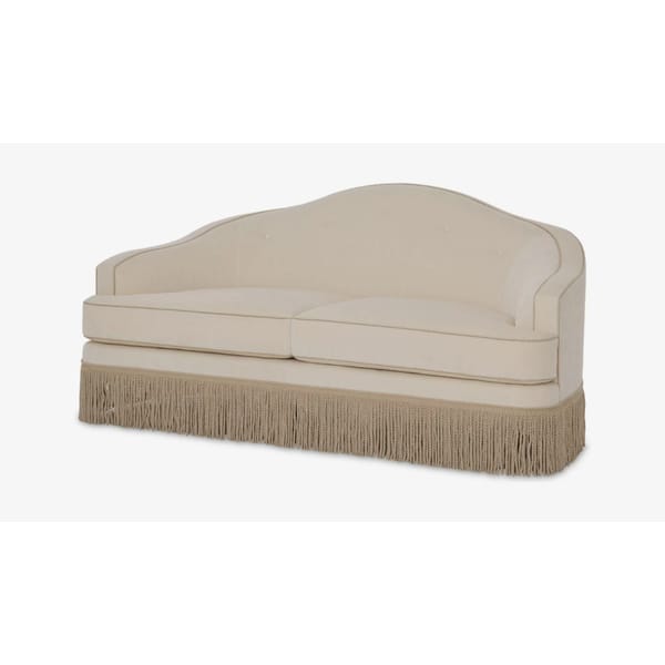 A cream-coloured Granny Sofa with a curved backrest, simple button detailing, and a long beige fringe along the base—perfect for adding vintage charm to your interior design. Set against a plain white background.