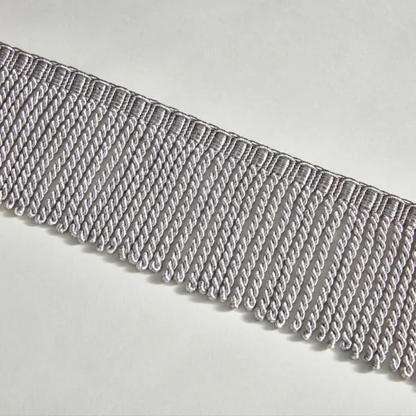 A close-up of a silver metallic fringe trim with twisted, looped threads, arranged in parallel rows on a white background—perfect for adding a touch of Granny Style charm to the latest sofa trends.