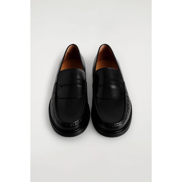 A pair of classic black leather loafers with a rounded toe and low heel, displayed side by side on a plain light background—timeless footwear that’s a staple in style tips for men.