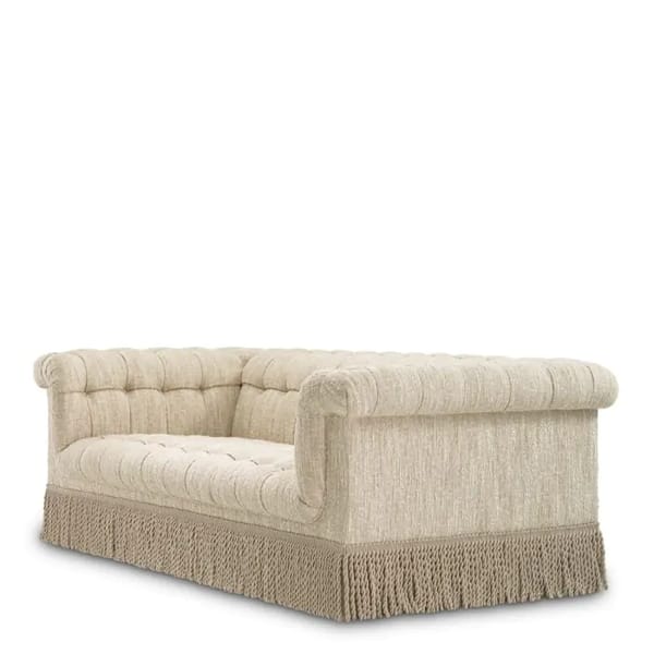 A cream-coloured, tufted Granny Sofa with rolled arms and backrest, upholstered in textured fabric. This vintage furniture piece features a decorative fringe along the bottom edge and is set against a plain white background.