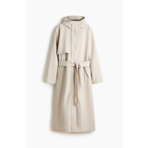 A long, light beige trench coat with a hood, front buttons, a tied waist belt, and side pockets—this piece channels the elegance of stylish waterproof jackets, displayed against a plain white background.