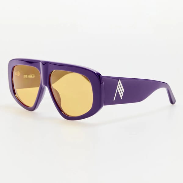 Purple sunglasses with thick frames, yellow-tinted lenses, and a white diagonal-striped logo on the side, displayed against a plain white background.