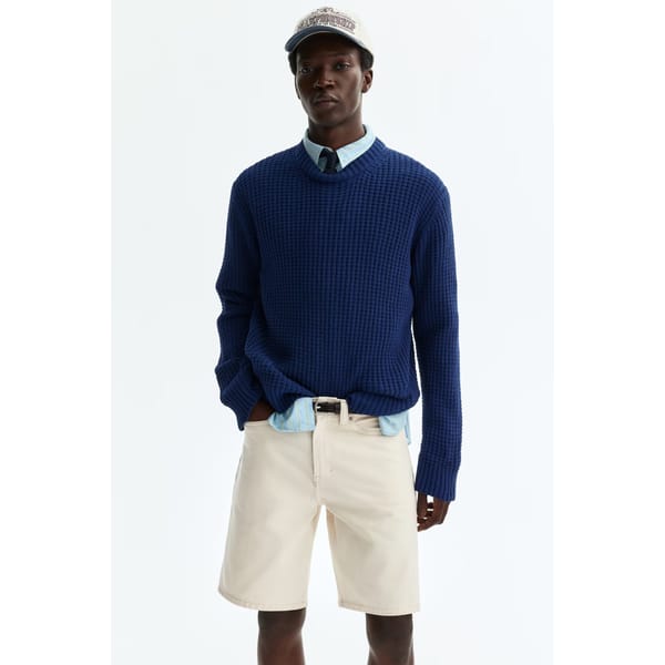 male model wearing cream cap, navy sweater and white Relaxed Fit Denim shorts