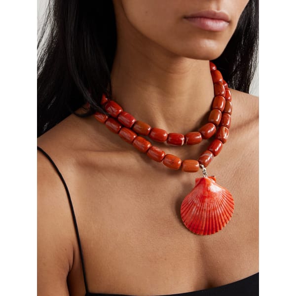 A woman wearing a black top and a three-strand red beaded necklace with a large red seashell pendant, perfect for adding a touch of statement jewellery to any look.