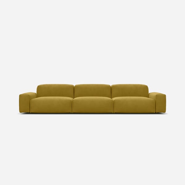 A modern, mustard yellow three-seater sofa with low, wide armrests and plush cushions, reflecting the chartreuse colour trend, set against a plain white background.