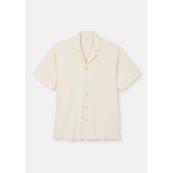 Cream-coloured, short-sleeve button-up shirt with a notched collar, displayed on a white background. The shirt has a simple, classic design with five buttons and a relaxed fit—perfect for men’s summer dressing and evoking the effortless elegance of The Talented Mr Ripley style.