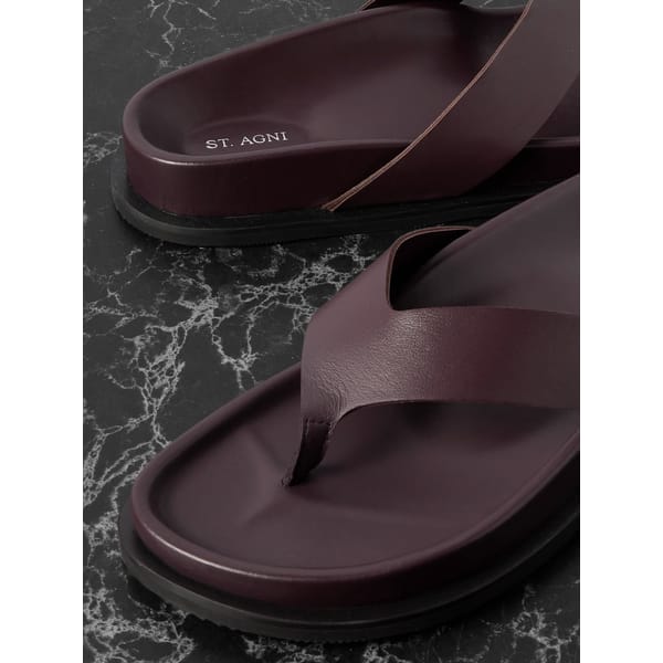 Close-up of maroon leather sandals with criss-cross straps, featuring ST. AGNI branding on the footbed, placed on a black marble surface—perfect for the summer sale season.