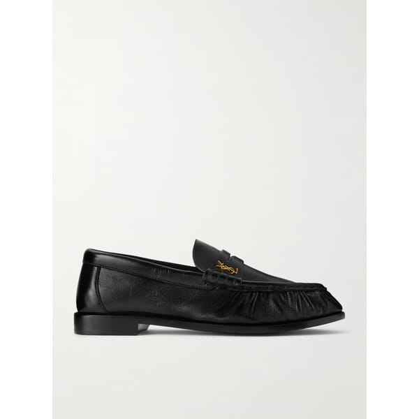 A pair of black leather loafers featuring a rounded toe, gathered detailing on the sides, and a gold Saint Laurent logo on the strap, displayed on a white background.