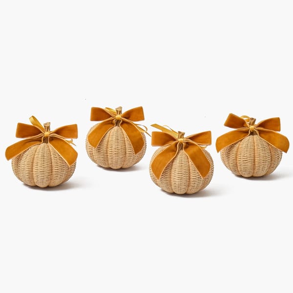 Four woven wicker pumpkins, each topped with a golden-brown velvet bow, perfect for autumn tablescape ideas.