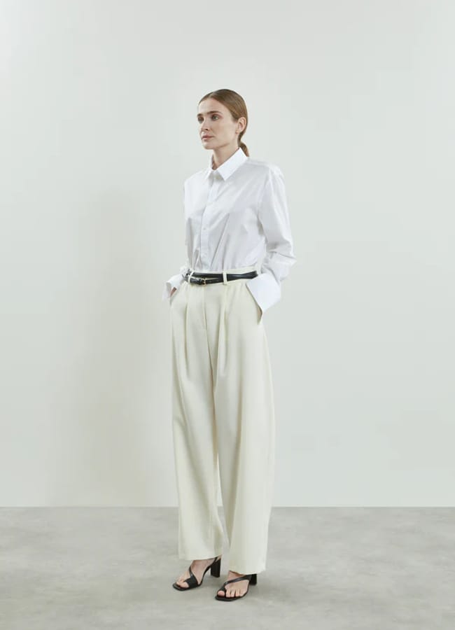 model wearing white sheer shirt and cream trousers