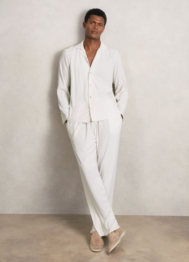 male model wearing Reiss Aubry Plissé Cuban-Collar Long-Sleeve Shirt in Off White and trousers