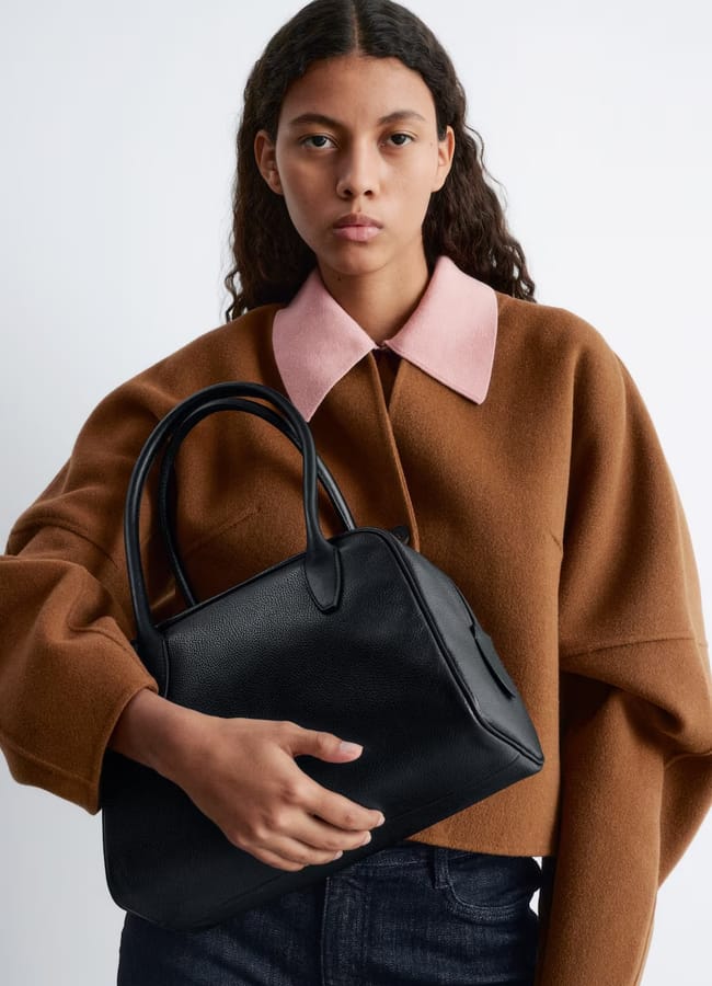 model wearing brown jacket holding black bowling bag