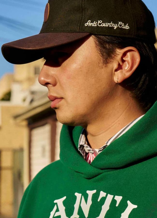man wearing anti country club cap and green hoodie