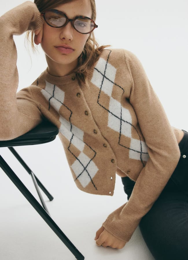 model leaning on chair wearing beige argyle cardigan