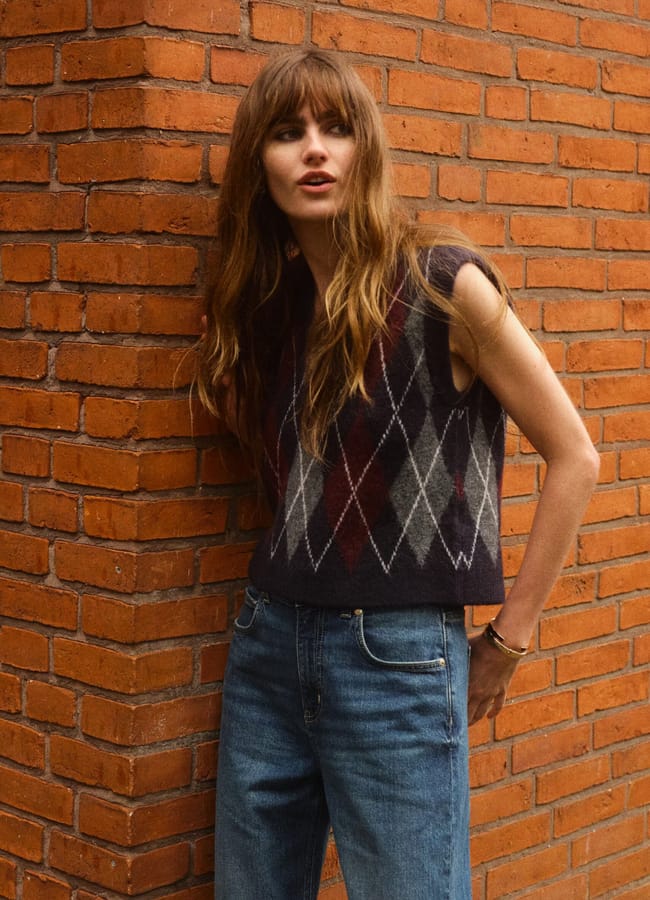 female model against wall wearing argyle knit vest and jeans