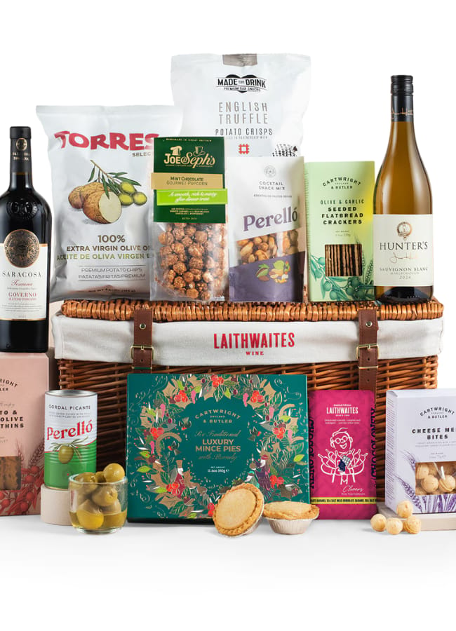 A wicker hamper filled with gourmet food and drink items makes the perfect Christmas hampers gift, featuring wine, crisps, biscuits, mince pies, nuts, olives, bread thins, cheese bites, popcorn and preserves displayed neatly around and inside the basket.