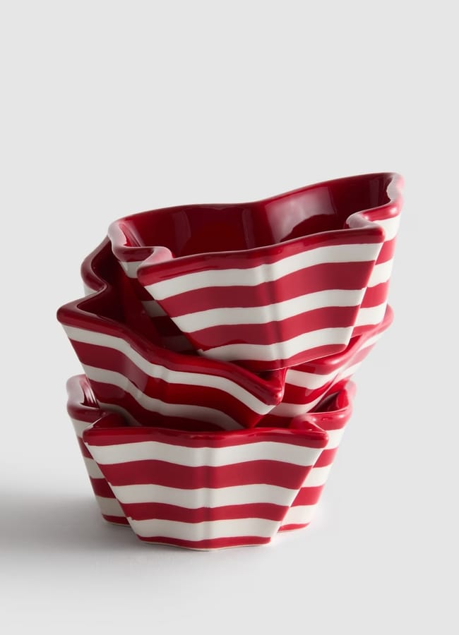Three red and white striped ceramic ramekins with wavy, fluted edges are stacked unevenly against a plain light grey background, perfect for adding festive charm to your Christmas tablescape.
