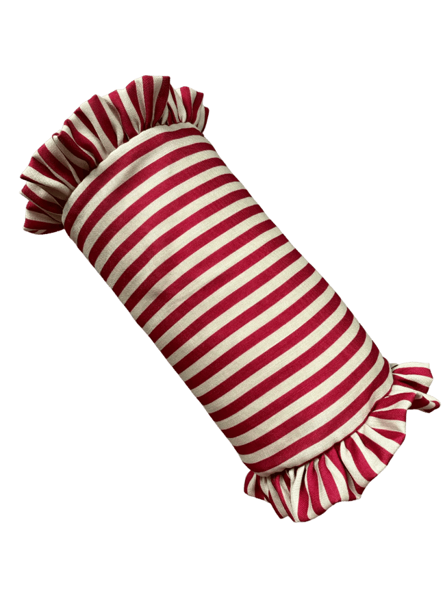 A cylindrical cushion with red and white horizontal stripes and ruffled ends, inspired by the Unexpected Red Theory, adds a playful pop to interior design, resembling a wrapped sweet.