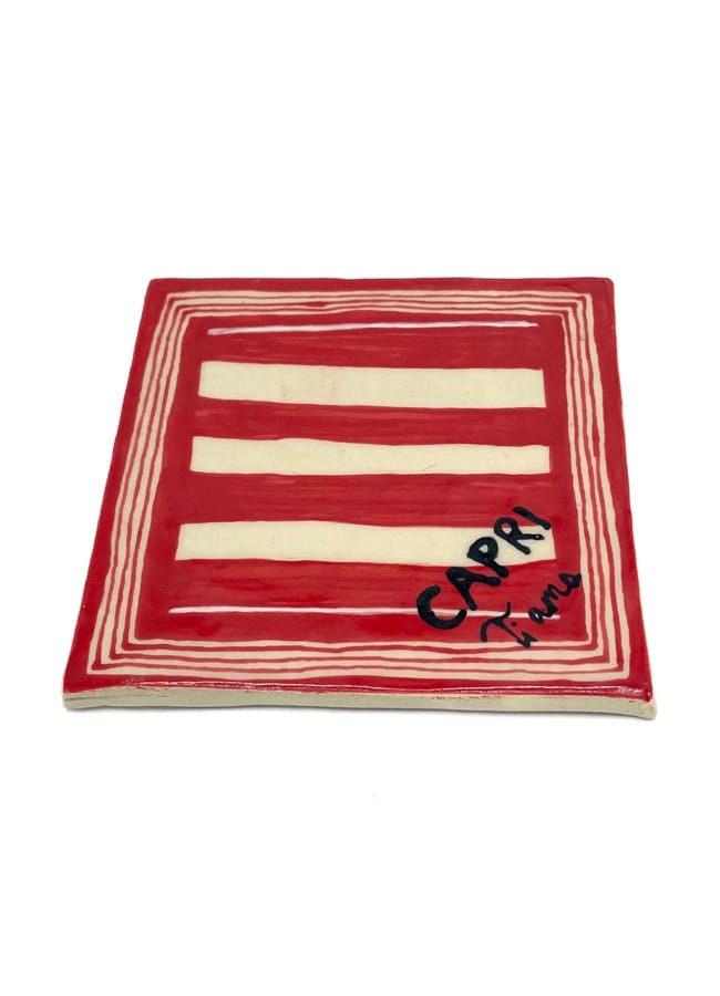 A square ceramic coaster with a red and white striped pattern, inspired by the Unexpected Red Theory, and the words CAPRI and ti amo handwritten in black in one corner—a charming accent for any 2026 interior design.