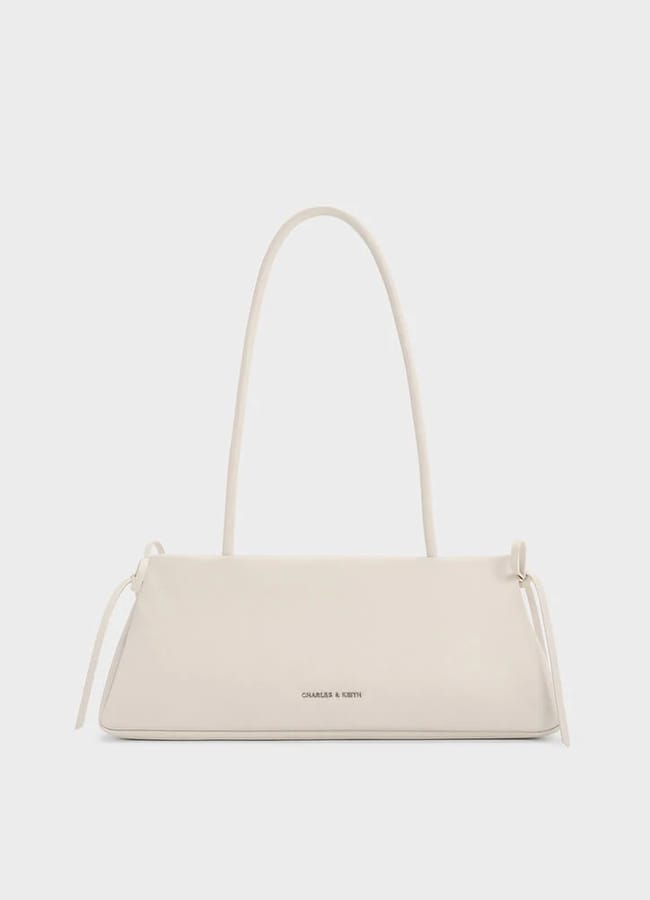 A minimalist, rectangular white handbag with a long strap and subtle side ties, featuring the CHARLES & KEITH logo in small gold letters—perfect for pairing with brown trousers for an effortlessly chic fashion statement.
