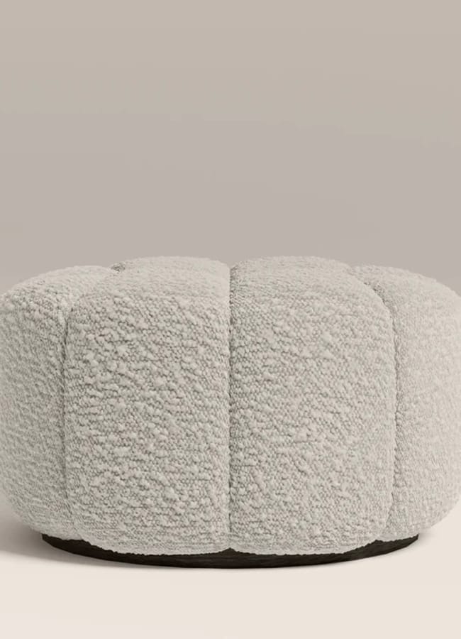 A round, light grey, textured ottoman with a plush, segmented design sits on a plain background—perfect for adding cosy home vibes to your home decor.