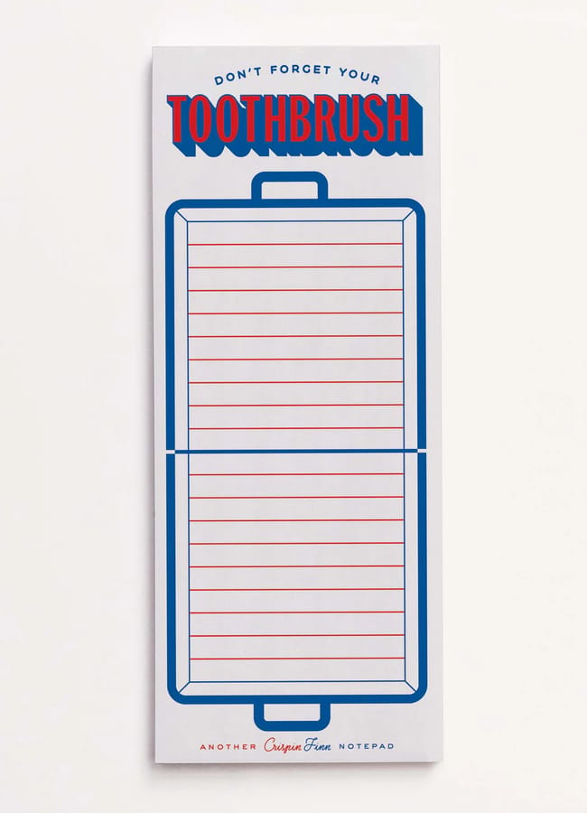 A notepad designed like a suitcase with red lines and blue borders, reminiscent of 2026 diaries. At the top, it says Don't forget your TOOTHBRUSH in bold letters. The bottom reads, Another Crispin Finn Notepad.
