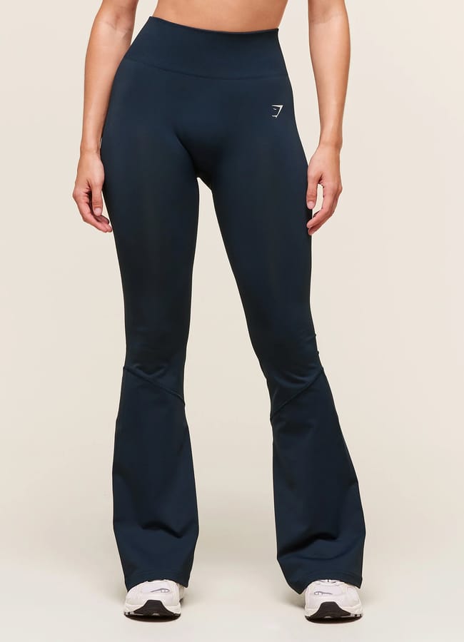A person wearing high-waisted, navy blue flared leggings from the latest activewear collection and white trainers stands against a plain light background. Their arms are relaxed at their sides, with the upper body cropped out of the image.