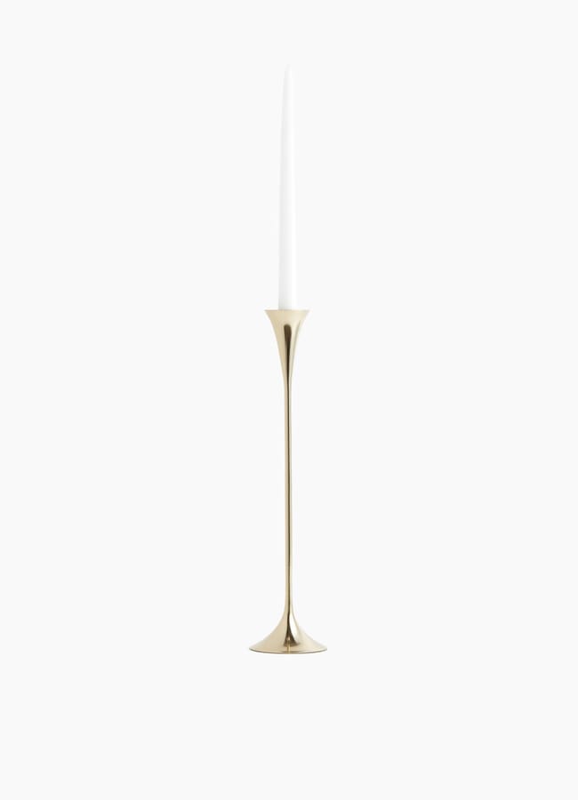 A tall, slender gold candlestick holder with a flared base holds a single white taper candle, perfect for elevating your Christmas tablescape against a plain white background.