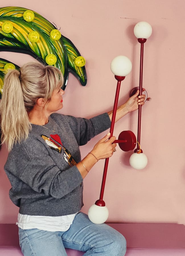 A woman with blonde hair in a ponytail inspects a modern red light fitting, embodying the 