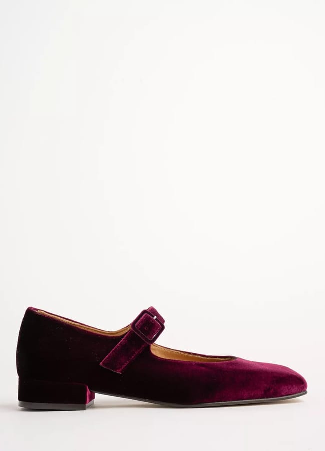A single burgundy velvet Mary Jane flat shoe with a low heel and a strap across the instep, reminiscent of festive elegance for a Christmas tablescape, displayed against a plain white background.