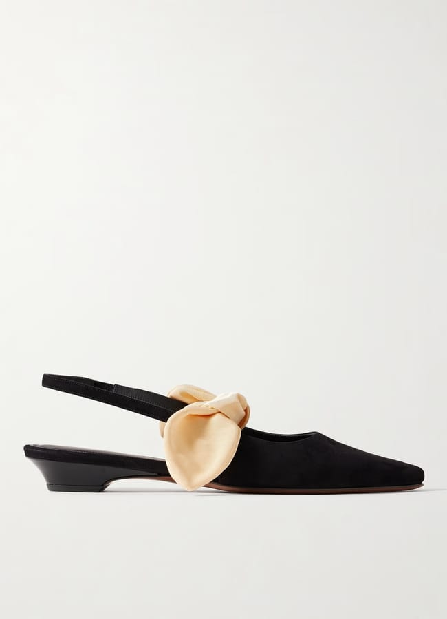 A black slingback kitten-heel shoe with a pointed toe and a large, pale yellow decorative bow on the side embodies elegant bow fashion, set against a plain white background.