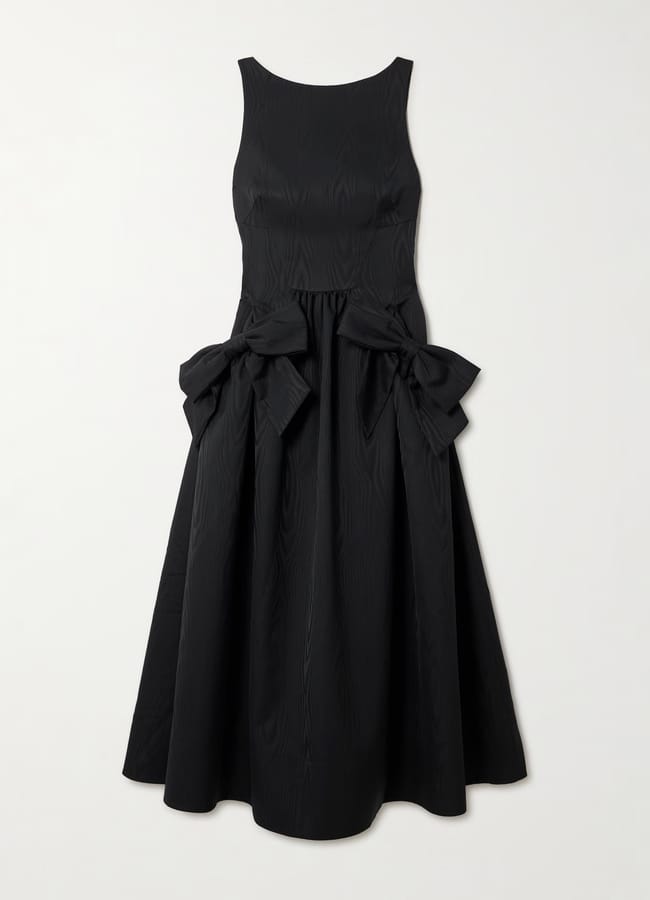 Sleeveless black midi dress with a fitted bodice, full skirt, and two large decorative bows at the waist highlights bow fashion. The subtly textured fabric adds depth. Set against a plain white background.